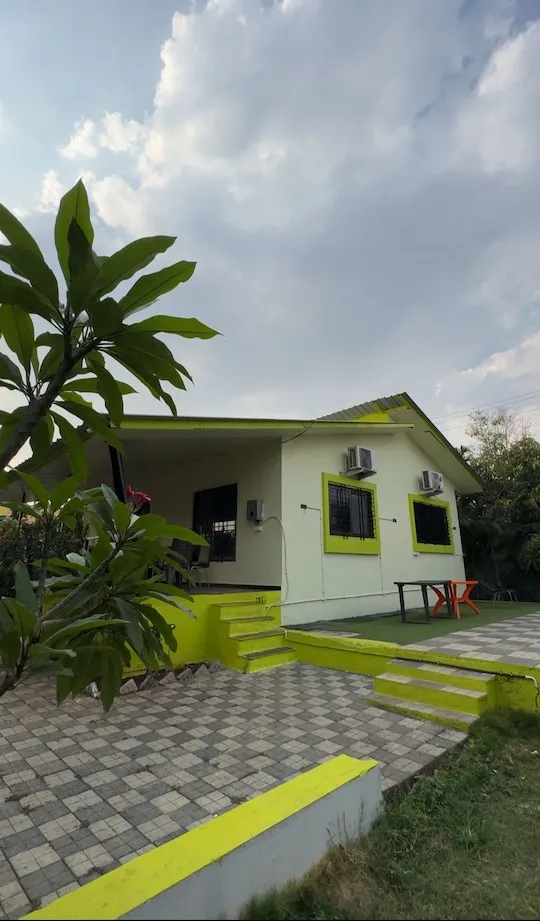 Green-trim facade and frangipani — PN Nature's Paradise Villa, Igatpuri
